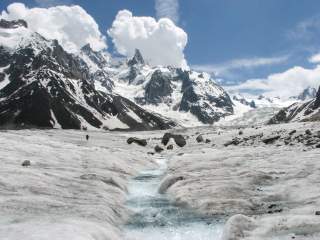 Auf einem Gletscher läuft in der Ferne ein Mensch, im Hintergrund hohe, steile Bergmassive.