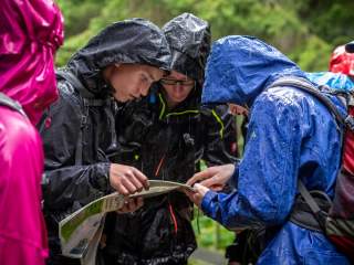 Drei Menschen in Regenbekleidung studieren im Regen eine Karte