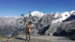 Mädchen hebt Mountainbike in die Luft vor Bergkulisse