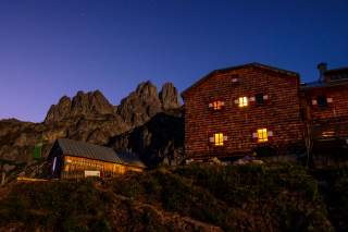Hütte bei Nacht mit Sternenhimmel und Bergen