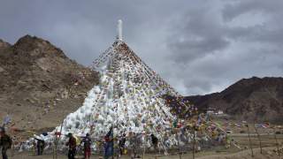 Eine Eis-Stupa ist mit bunten Fähnchen geschmückt. Rundherum ist nur braunes Gestein zu sehen.