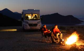 Ralf Dujmovits und Nancy Hansen sitzen am Lagerfeuer, im Hintergrund steht ihr Wohnmobil.