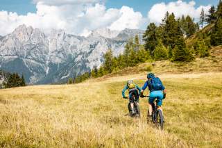 Zwei Mountainbiker fahren über eine Wiese in Richtung Civetta