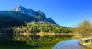 Ein Bergsee, in dessen Wasser sich Bäume und die felsigen Gipfel spiegeln.