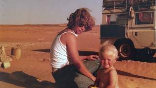 Astrid sitzt neben ihrer Mutter im Sand. Im Hintergrund der bepackte Geländewagen.