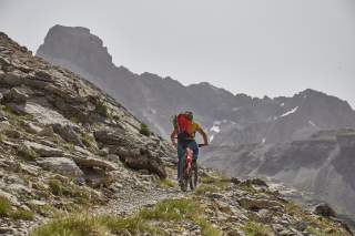 Mountainbiker auf Bergweg mit Rucksack und Kletterzeug