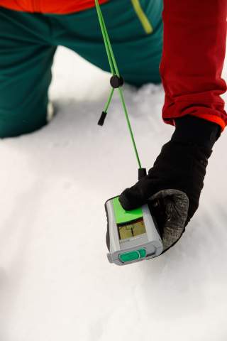 Hand mit Lawinenverschüttetensuchgerät (LVS) auf Schnee