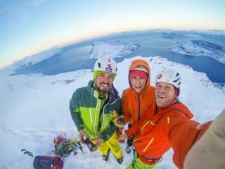 Drei Männer ins Eiskletterausrüstung machen ein Selfie. Im Hintergrund sieht man Schnee, Eis und das Meer.