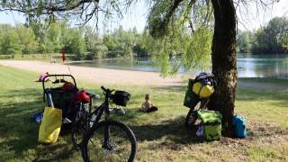 Nelion sitzt an einem See, im Vordergrund das bepackte Fahrrad.