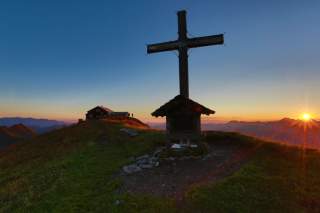 Hütte und Gipfelkreuz im Sonnenuntergang