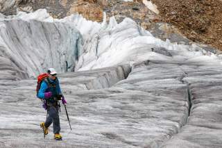 Mann läuft mit Stöcken und Steigeisen über Gletscher