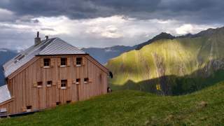 Eine Alpenvereinshütte in dramatischen Lichtverhältnissen im Hochgebirge. Im Hintergrund scharfe Berggrate.