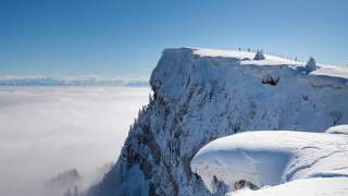 Felsgipfel vom Schnee bedeckt, im Hintergrund die verschneite Alpenkette.