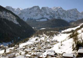 Das verschneite Dorf Lungiarü vor steilen Bergen, der Puezgruppe in Italien.