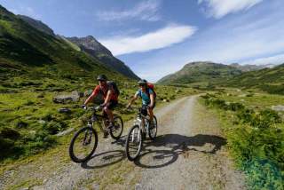 Zwei Menschen auf Mountainbikes fahren am Berg auf Forstweg