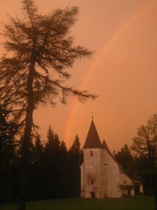 Alte Kirche in orangem Gewitterlicht mit Regenbogen