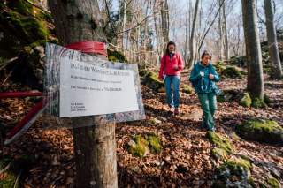 Zwei Frauen wandern in herbstlichem Wald, im Vordergrund ein Sperrschild für einen Felsen
