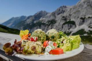 Spinatknödel angerichtet mit Salat auf Teller vor Bergkulisse