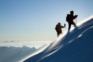 Zwei Menschen kämpfen sich im Wind steilen Schneehang hoch