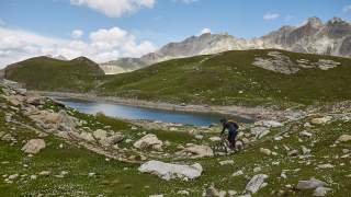 Mountainbiker auf Trail in Wiese vor Bergsee