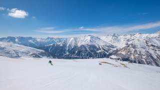 Skifahrer bei Abfahrt mit Ausblick auf zahlreiche Gipfel