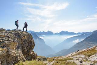 Zwei Menschen stehen in den Bergen auf Fels mit Aussicht über Gipfel