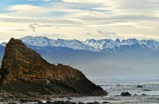 Fels an der Küste mit Blick auf schneebedeckte Bergkette