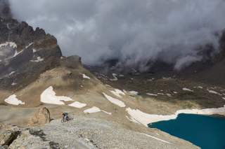 Mountainbiker fährt auf Trail neben Bergsee, der Himmel ist mit dunklen Wolken bedeckt