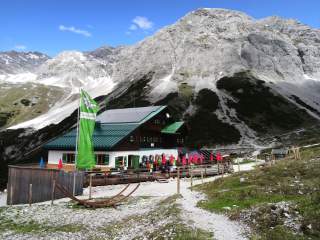 Hütte mit roten Sonnenschirmen vor felsigem Gipfel