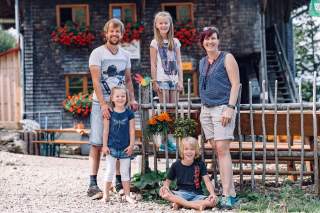 Ehepaar mit drei Kindern steht vor Berghütte
