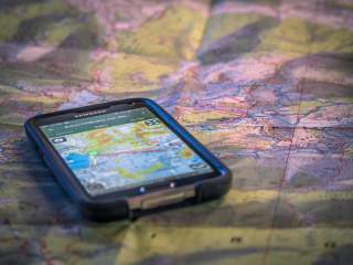 Smartphone mit Tourenapp liegt auf analoger Landkarte