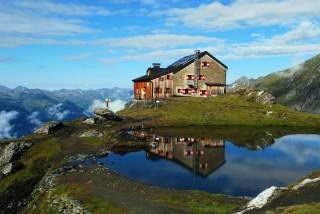 Eine Alpenvereinshütte spiegelt sich in einem kleinen Bergsee.