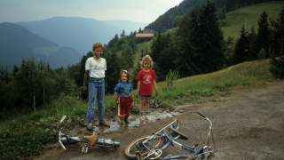 Vintage-Foto von drei Kindern im Matsch und ihren Fahrrädern davor auf dem Boden.