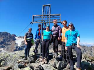 Gruppe an Gipfelkreuz bei blauem Himmel