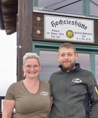 Paar steht vor Hütte mit Schild Hochrieshütte