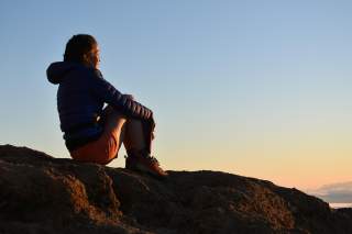 Frau sitzt auf Felsen im Sonnenuntergang