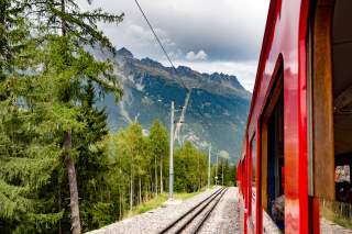 Ein roter Zug vor Bergkulisse, Blick aus dem Fenster.