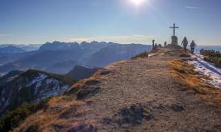 Menschen auf Gipfel mit Kreuz und Aussicht auf Bergketten