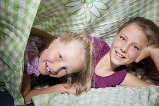 Zwei Mädchen in grün-weiß-karierter Bettwäsche, auf der ein Edelweiß-Logo vom Alpenverein gedruckt ist.