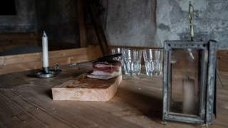 Eine alte Kerzenlaterne steht auf dem Tisch, daneben Wassergläser und ein Holzbrett mit Schinken.