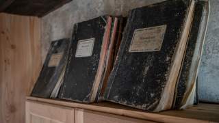 Mehrere alte, abgegriffene Hüttenbücher stehen auf einem Holzregal.