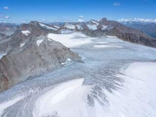 Weite Gletscherfläche mit Gletscherspalten, Alpenvereinshütte auf Felssporn, alpine Gipfel im Hintergrund