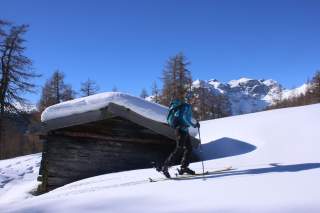 Skitourengeherin vor Holzhütte bei Sonnenschein