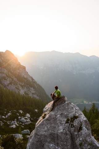 Mensch sitzt auf Fels bei Sonnenuntergang am Berg